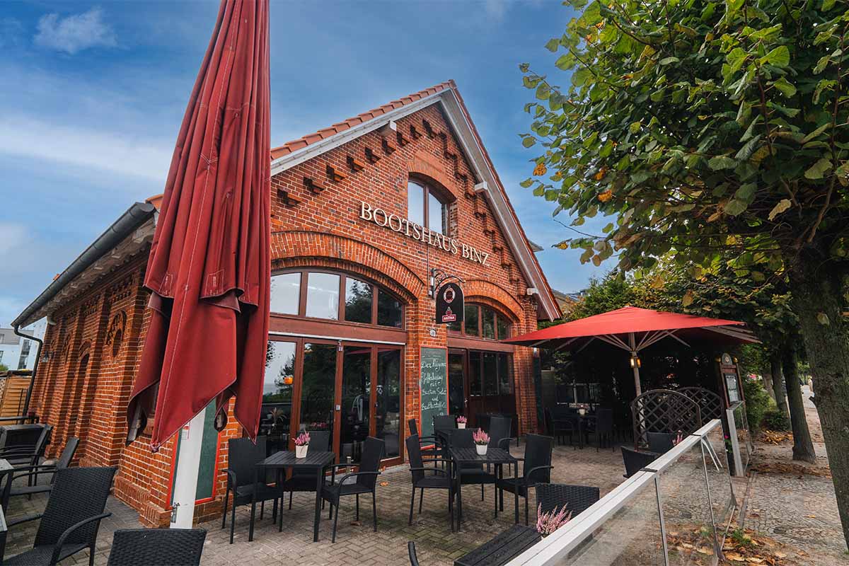 Backsteinfassade und Terrasse des Bootshaus Binz auf Rügen mit roten Sonnenschirmen und gemütlicher Atmosphäre.